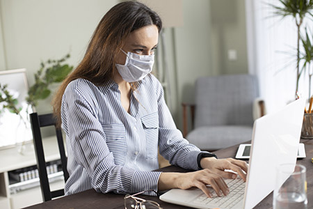 Woman wearing a mask while on her computer trying to sell her home, sell your home in a crisis concept